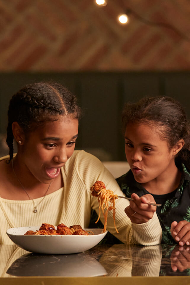 Two girls excitedly share a bowl of Bella Italia spaghetti and meatballs