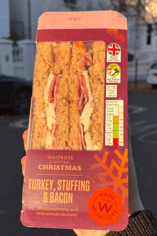 Hand holding turkey, stuffing and bacon Christmas sandwich from 2023